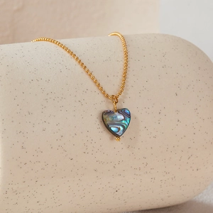 Macro shot of a heart-shaped abalone shell pendant on a golden bead chain