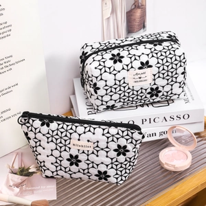 Black and white flocked floral fabric cosmetic bags on decorative book stacks