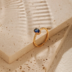 Macro view of a gold-plated open ring with an oval blue gemstone and textured band