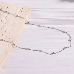 Detail view of a silver stainless steel bead chain necklace on a marble stone surface