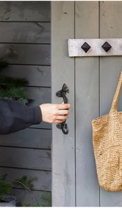 Detailed view of hand pulling a black cast iron seahorse handle on wooden door
