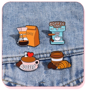 Detail of coffee enamel pins set on blue denim fabric featuring moka pot and croissant