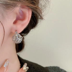 Detail view of silver hollow vintage basket earrings on female model with metallic texture