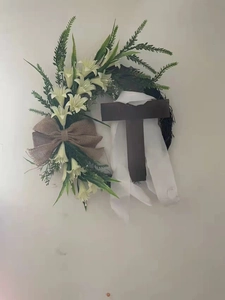 Detail of Easter cross wreath featuring white lilies and burlap bow on vine base