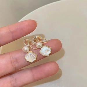 Detailed close-up of shell-shaped gold earrings with white baroque pearls and screw clips