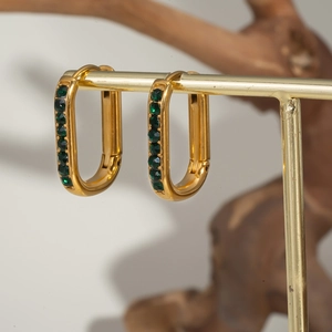 Detail view of U-shaped gold earrings with green emerald stones on a jewelry stand