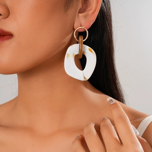 Detail of golden hoop earring with white resin pendant worn on model's ear