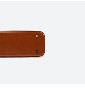 Detail shot of brown leather bag base with protective dark metal feet and fine stitching
