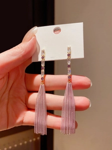Detail of pink tassel earrings with purple and white gemstones held by a model