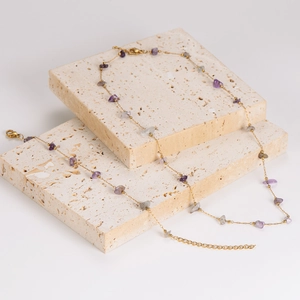 Gold chain necklace set with purple and grey crushed stones on a stone display