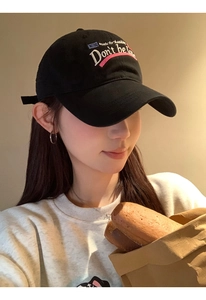 Detail of pink and blue embroidery on black cotton baseball cap worn by a female model