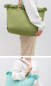 Detail of woven tote bag with fringe trim, leather handles in green and light blue