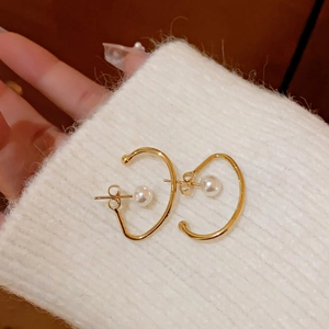 Macro shot of gold-finished C-shaped pearl earrings on white knit sweater texture