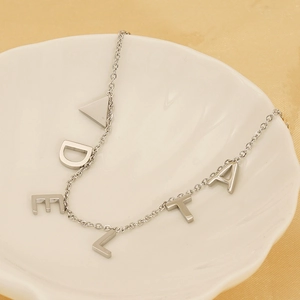Detail of silver titanium steel necklace featuring DELTA letter pendants on a white plate