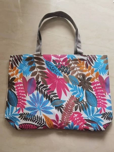 Detail of canvas tote bag featuring colorful botanical leaf patterns and gray handles