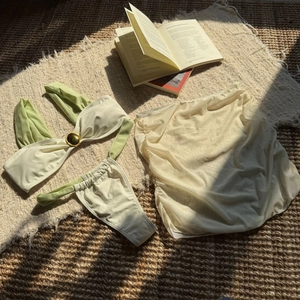 Detailed flat lay of cream and sage green bikini set with mesh skirt and metal buckles