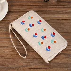 Detail view of cream embroidered long zip wallet with floral patterns and wristlet strap