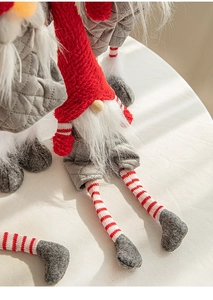 Close-up of knit Christmas gnome ornaments with red hats and striped legs on a soft white surface