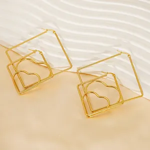 Macro shot of gold geometric layered heart earrings on a minimalist textured background