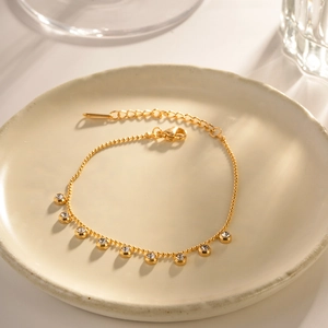 Gold-plated stainless steel bracelet with cubic zirconia charms on a ceramic tray