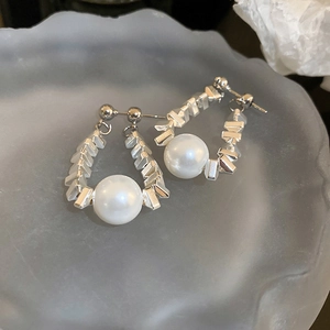 Macro detail of silver geometric beads and a white pearl on a minimalist stud earring