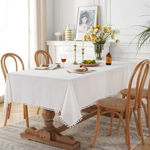 Modern white cotton tablecloth with pom-pom fringe edge on a wooden dining table