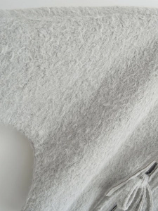 Detailaufnahme von lichtgrauem Wollstoff mit eleganten Fransen am Saum des Mantels