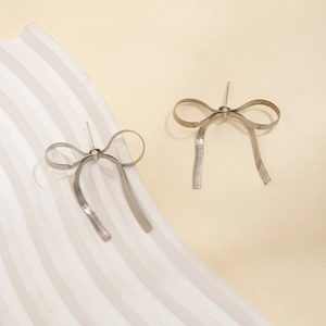 Detail of silver bow earrings with textured snake chain metal ribbon design on white tray