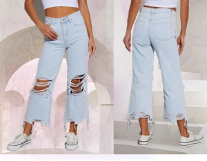 Dettaglio dei jeans in denim azzurro a gamba larga con strappi e dettagli consumati