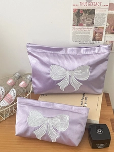 Detailed view of two-piece purple satin pouches with elegant white bow embroidery