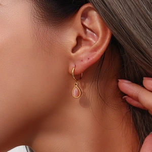Close-up of golden hoop earring featuring a pink teardrop opal pendant on a model