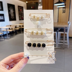 Set of four unique metal brooches with pearls and crystals shown on card packaging