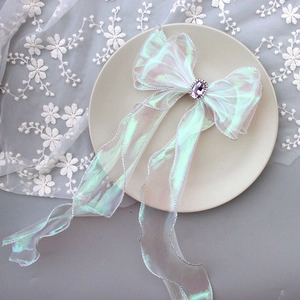 Detail of white organza bow hair clip with silver edges and purple gemstone center