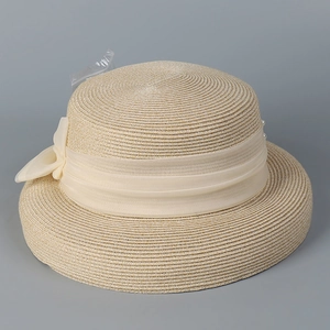 Close-up of beige woven straw hat with chiffon bow ribbon and pearl embellishment