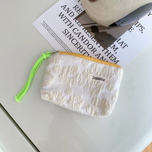 Detail of white floral jacquard makeup bag with yellow zipper and neon green lanyard