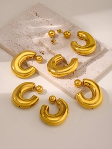 Detailed view of C-shaped hollow gold earrings and ball studs on textured stone display