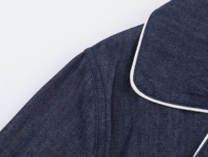 Detailed macro shot of dark blue denim shirt with white contrast piping and fine stitching