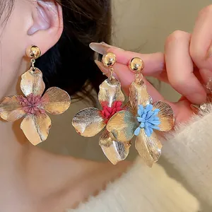 Oversized gold metal flower drop earrings with colorful centers worn by a model