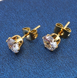 Detalle macro de pendientes de acero dorado con circón engastado en seis garras