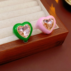 Macro detail of heart-shaped crystal rings with green and pink enamel finish in a box