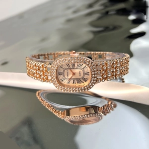 Close-up of elegant rose gold oval watch with crystal inlay on a reflective surface