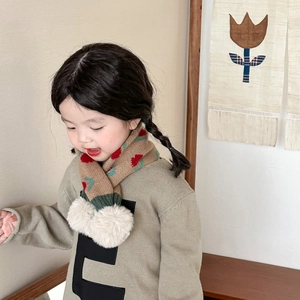 Detail of beige knitted kids scarf with red flower patterns and white pom-poms