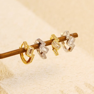 Close-up of gold and silver earrings with rectangular crystals on a wooden stand