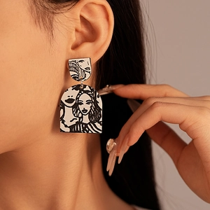 Close-up of black and white acrylic earrings featuring pop art portrait illustrations