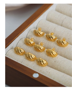 Detailed view of nine gold-plated twisted C-shape earrings on linen jewelry box lining