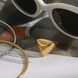 Nahaufnahme eines goldenen geometrischen Dreieckrings und Armreifen auf einem Magazin
