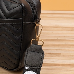 Close-up of black V-quilted leather bag with golden hardware and woven strap