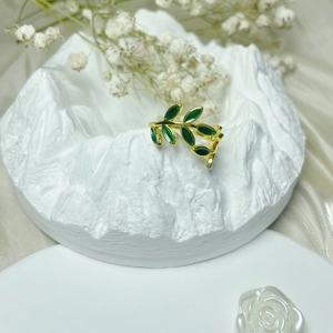 Detail of elegant gold copper ring with green enamel leaf design on plaster stand