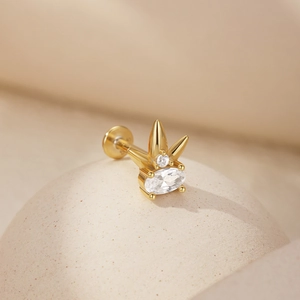 Detail of s925 silver stud earring with oval zircon and gold finish on beige prop