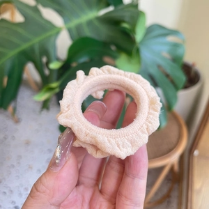 Elegant cream ruffled fabric scrunchie held against a natural green plant background